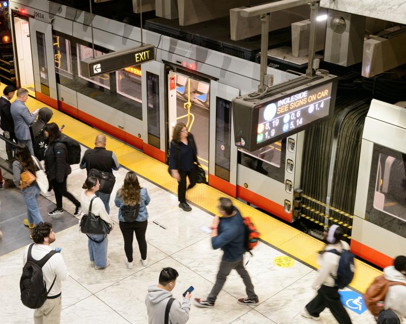 people walk around a metro station while a train pulls in 