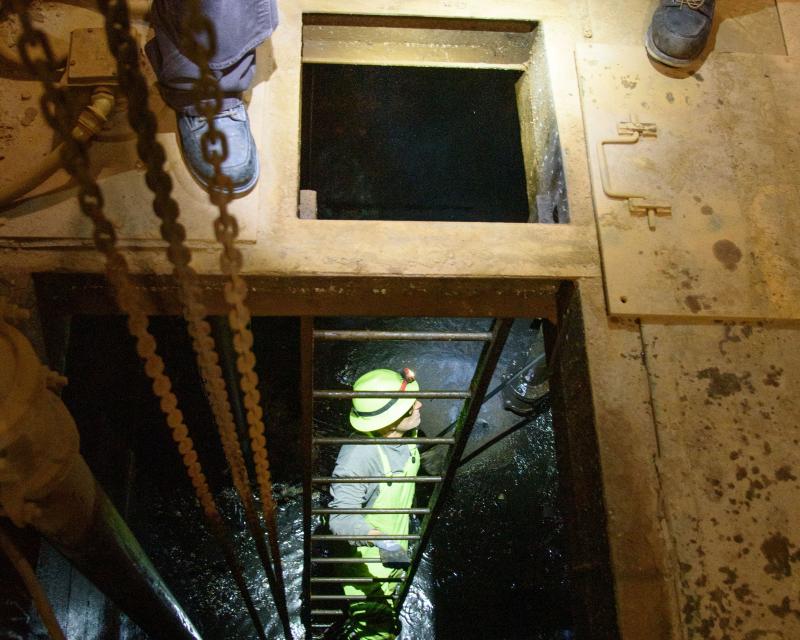  Person on a ladder in a hole underneath a wooden floor.    