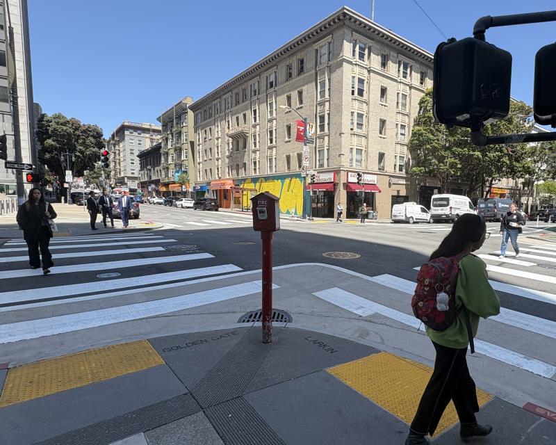 Pedestrians using new crosswalk at Larkin and Golden Gate intersection. One person waits near the traffic signal near the yellow tactile domes in the curb ramp leading to the crosswalk.