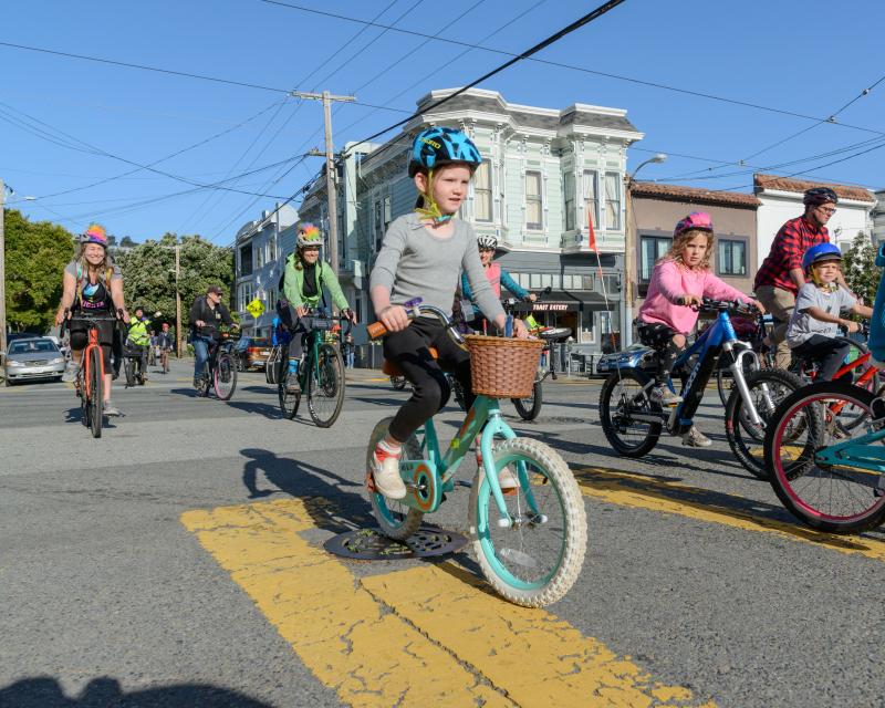 Students wearing helmets bike on a street for a school event.