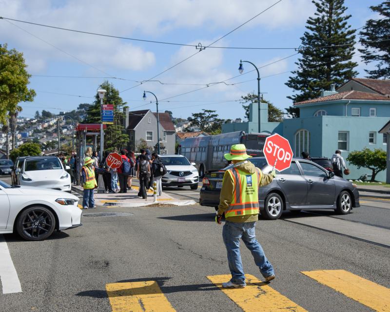 Crossing guard, cars and pedestrians in an intersection.