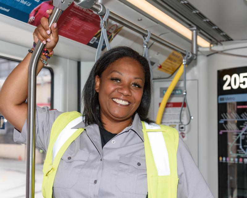 A woman in a grey shirt and bright yellow vest standing on a transit train