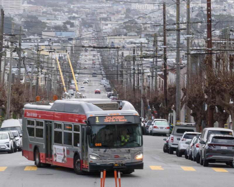 A bus drives down the street with parked cars on either side