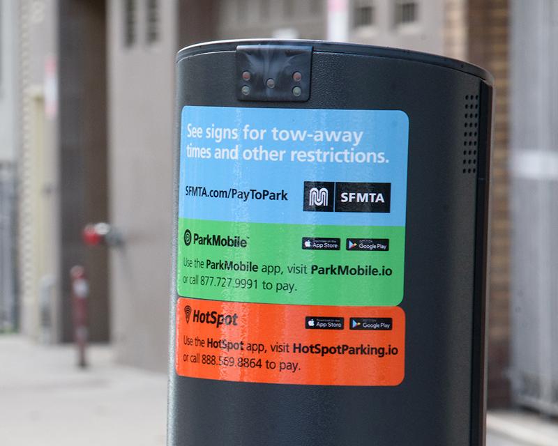 The backside of a parking meter with stickers showing mobile payment options