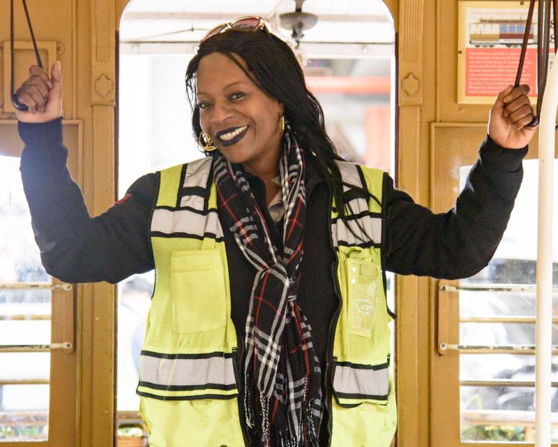 A person wearing a yellow vest standing on a cable car with her arms raised.