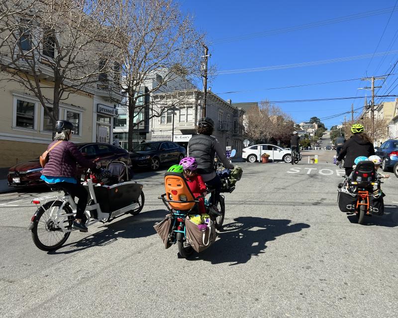 Adults and small children riding electric bikes in a street