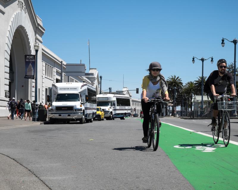 A person bicycling towards the camera in the green bike lane on the Embarcadero's roadway