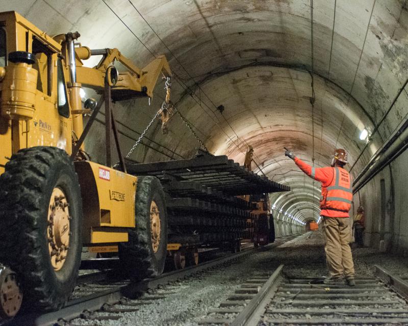 worker directing large machine lifting old track section inside Sunset Tunnel