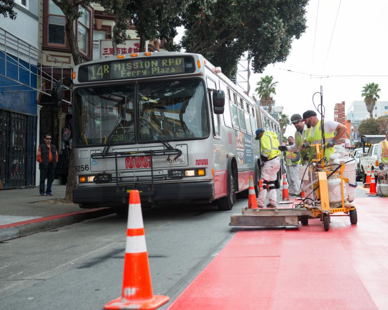 Crew placing red transit only lanes next to a 14R bus