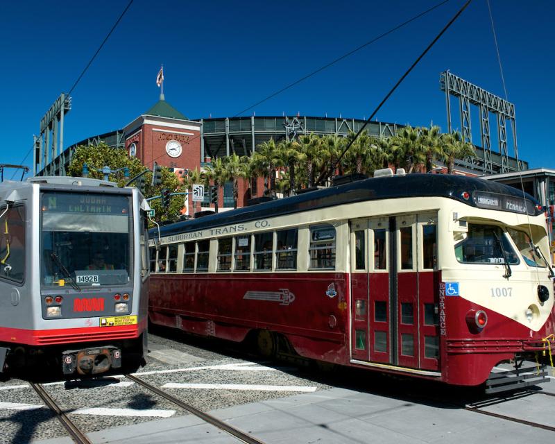 a rail train and a street car pass AT&T park
