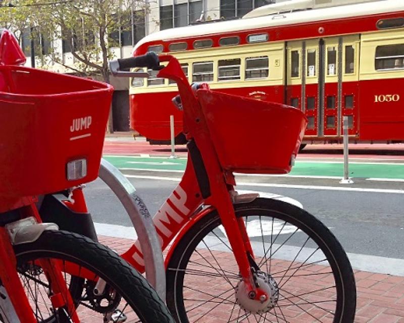 Two JUMP Bikes parked by a historic trolley. 