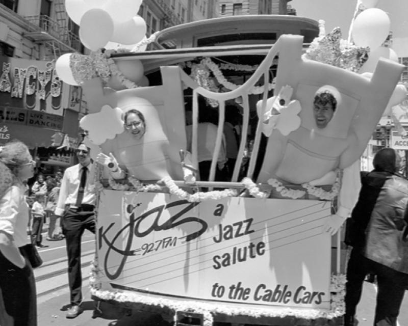 people dressed in costumes representing golden gate bridge on rear end of cable car
