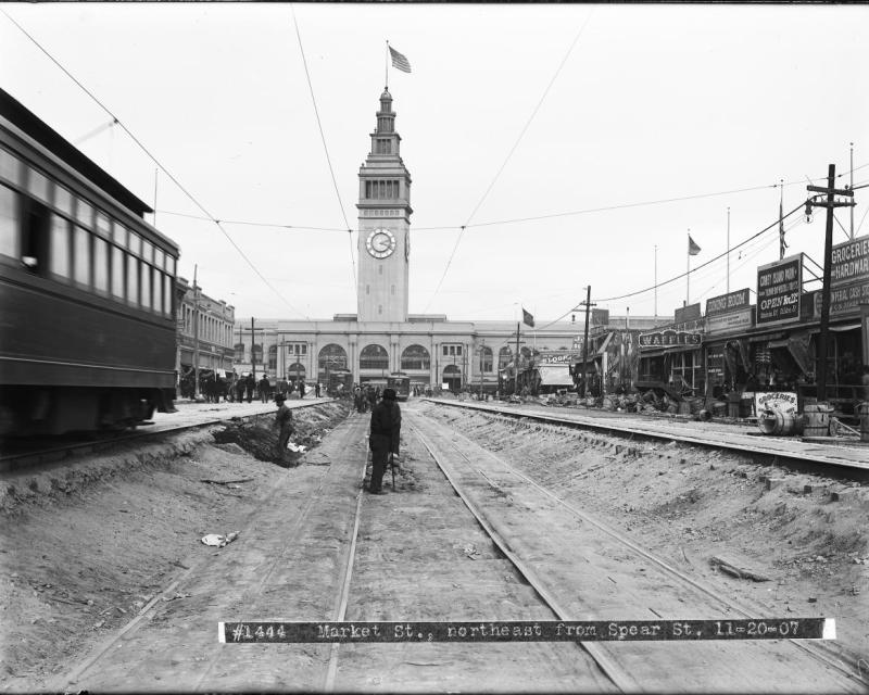 work men standing in sunken road with ferry building in background.