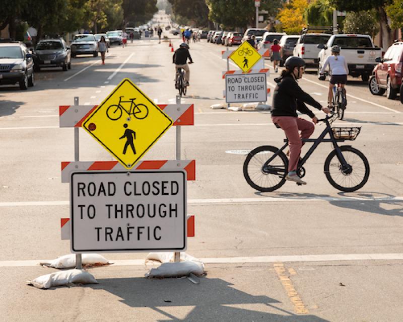 Image of temporary barriers in the travel lane stating "road closed to through traffic" with three bicyclists using the street