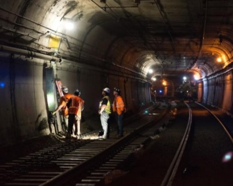 Photo showing 4 construction crew members working in subway tunnel on electrical connections