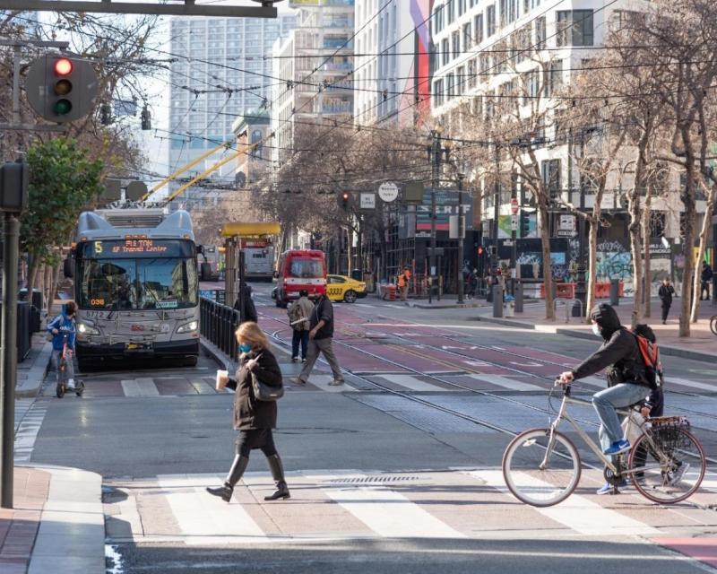 Photo of Market Street intersection with 5 Fulton bus, pedestrians, people on bicycles, a taxi, an ambulance, bikshare station, 