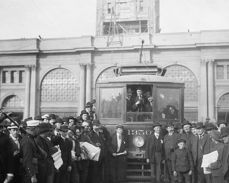 May 2, 1906 photo of first streetcar to run on Market Street showing front of streetcar and crowd of people around, with Ferry B