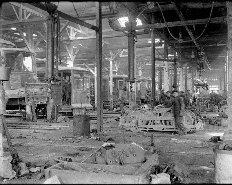 A view inside the overhaul shop in 1912 showing a row of streetcars at left and staff tearing down trucks and motors at right.