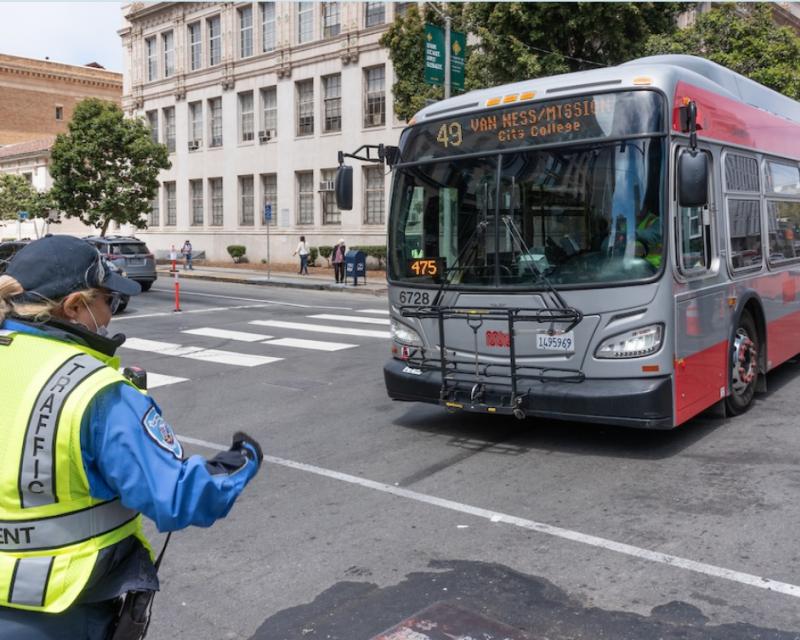 A traffic control officer guides a 49 Van Ness bus across an intersection