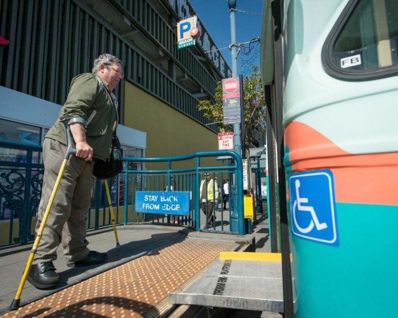 Bob Planthold boarding the F train via an accessibility ramp in his signature bright yellow crutches 
