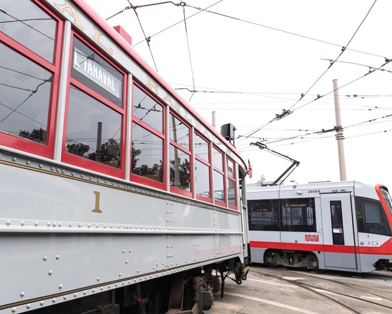 Muni streetcar 1 and new light rail vehicle in yard, both painted grey and red.