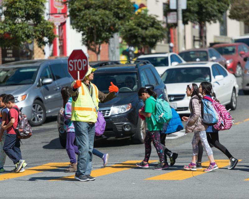 Crossing guard in the crosswalk holding a STOP sign with several children  walking 