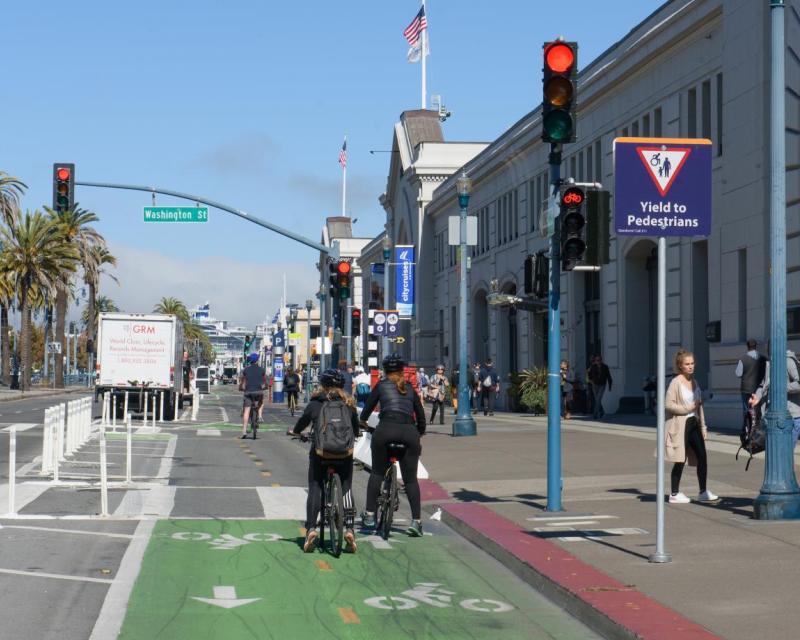 Bike riders and pedestrians seen on a city street's two-way bike lane at an intersection's red light