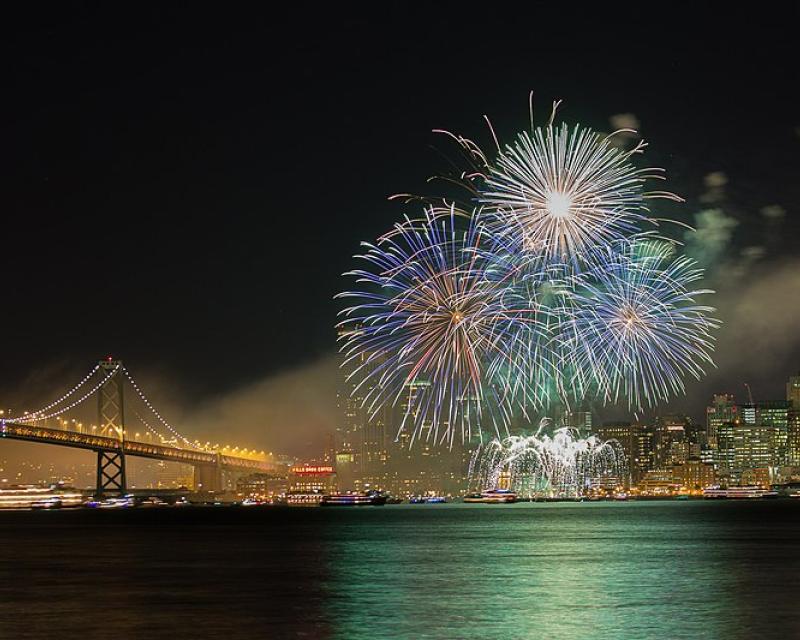 Fireworks over the the vary with a lighted city skyline and bridge in the background 