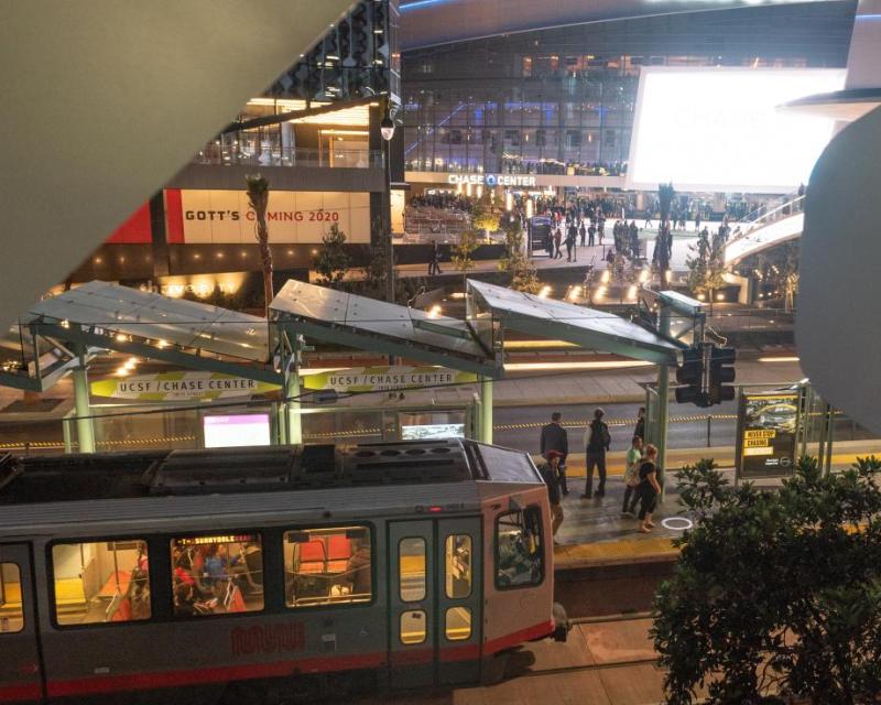  Photo of a Muni Metro train at the UCSF/Chase Center platform with Chase Center in the background.