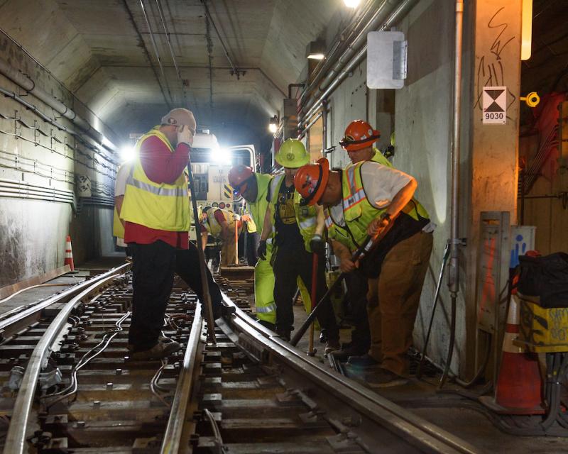 Several crew in safety gear standing over a rail track with tools angled in hand. 