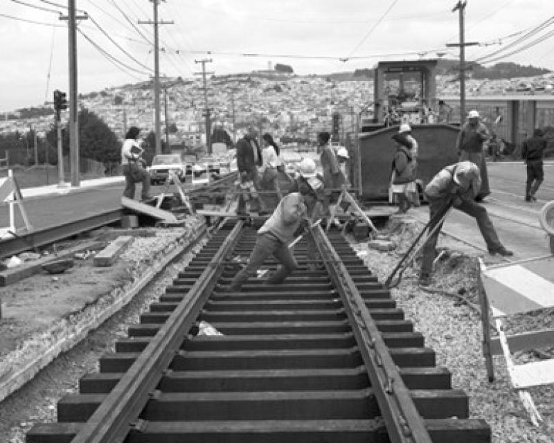 Group of people working on tracks, one pushes a rail while the other lifts a tie into place
