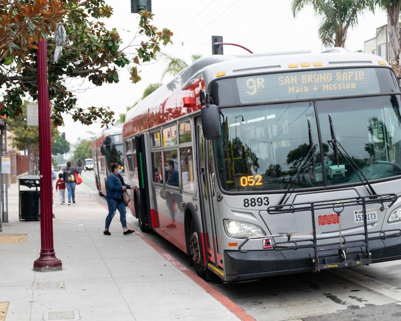 Person boarding a bus from a bus stop on the sidewalk with an adult and child walking down the street