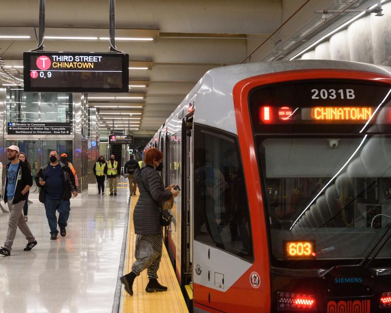 A train is pulled up alongside a metro station platform. One passenger is seen boarding. 