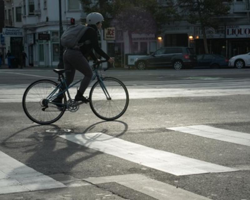 A bicyclist with a backpack and helmet is seen in the street adjacent to a crosswalk. 