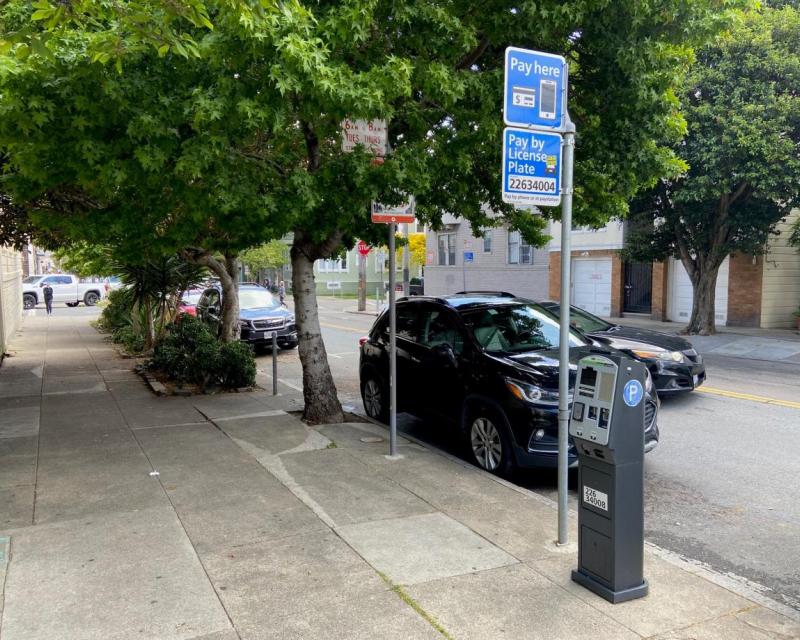 Cars outside near sidewalk with trees and parking meter pay station.