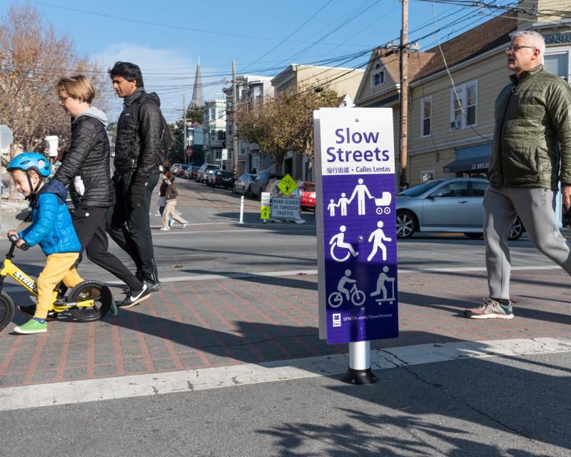 Slow Streets sign and people crossing the street