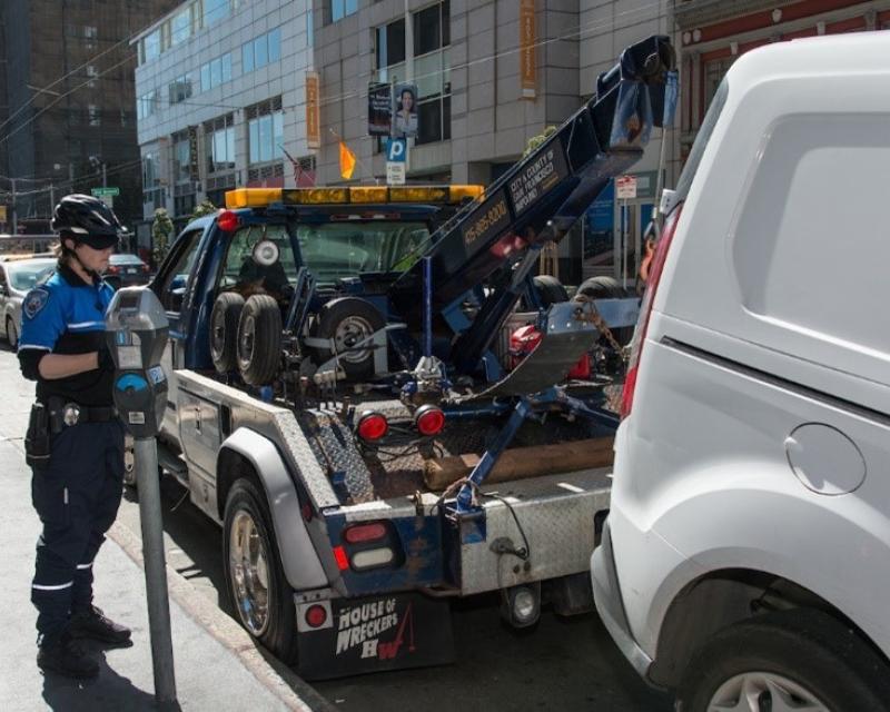 A tow truck, a car and an officer by parking meters at the curb 