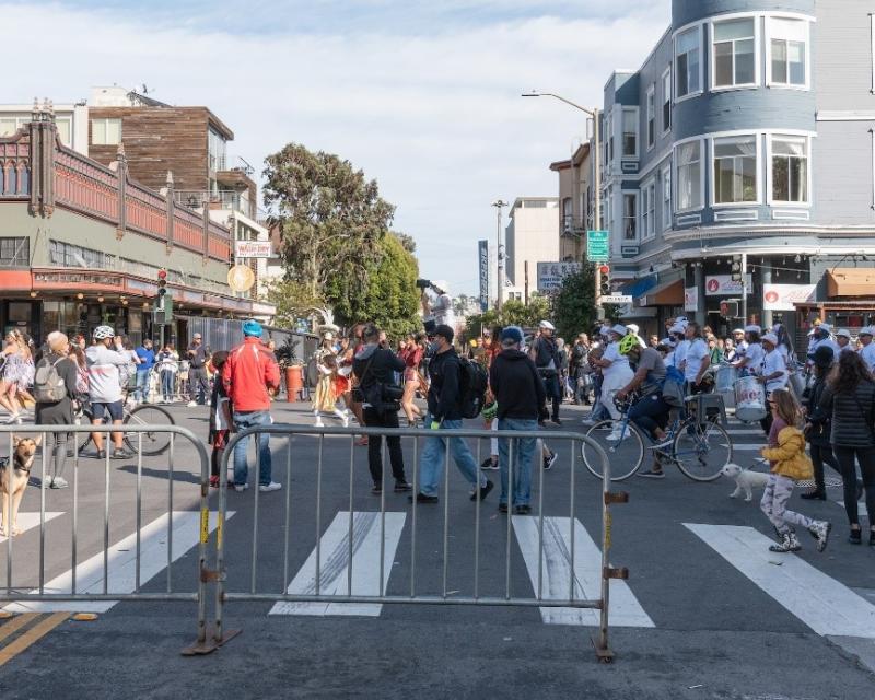 A large crowd of people at a street fair with blockades at the crosswalk.