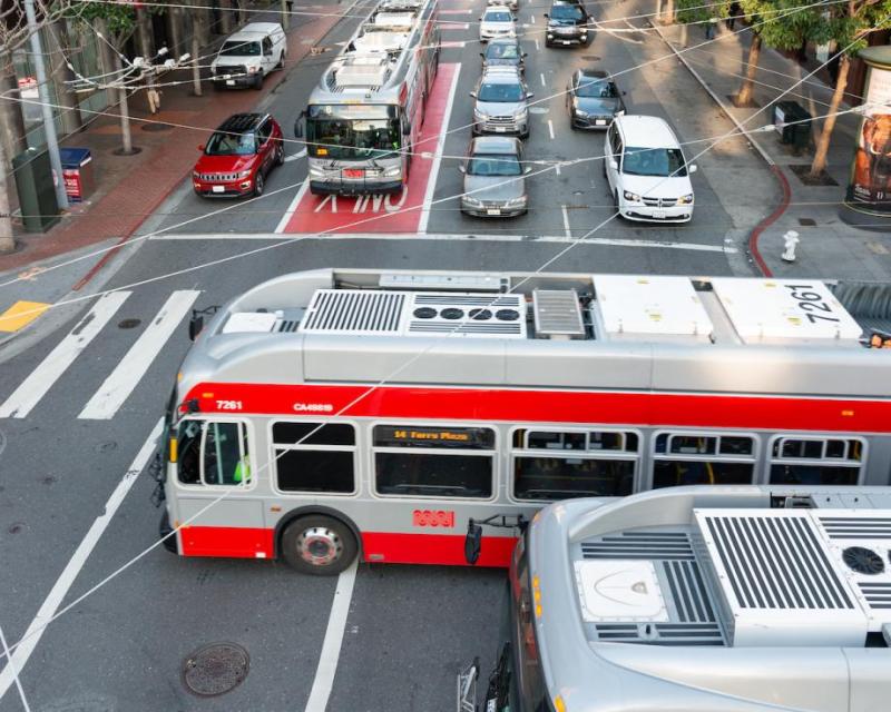 Buses and cars at an intersection with overhead wires.