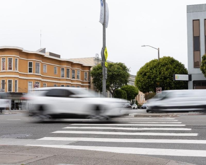 A white car appears blurry as it speeds through an intersection.