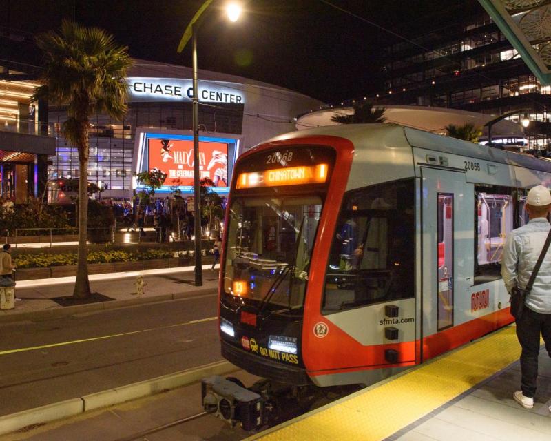 A light rail train stopped at a platform in front of the Chase Center arena in San Francisco.