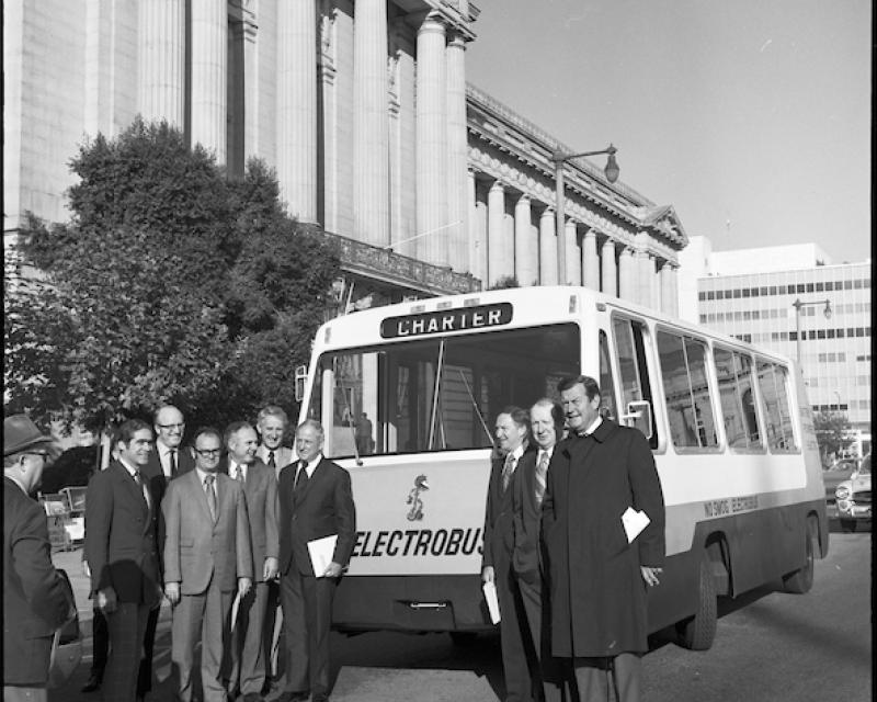 A black and white photo of an early stage Electrobus with a group of people posing for a photo.