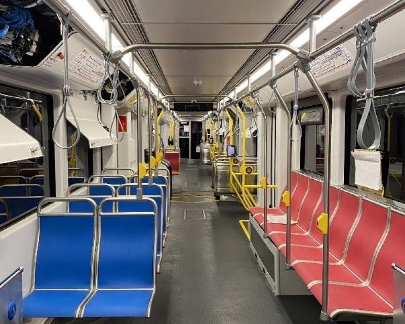 The interior of a train with blue double seats facing forward on one side and a row of red seats facing the aisle on the other.