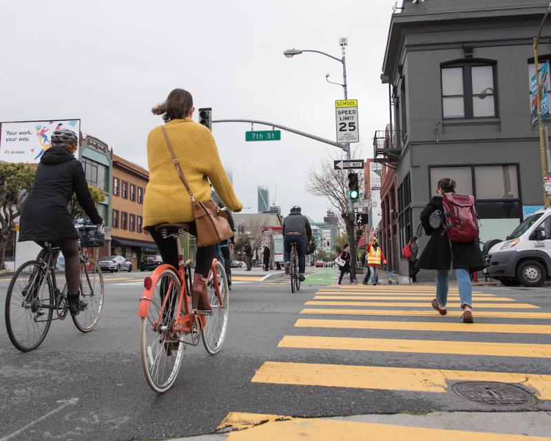 People walking and on bicycles in the street and crosswalk.