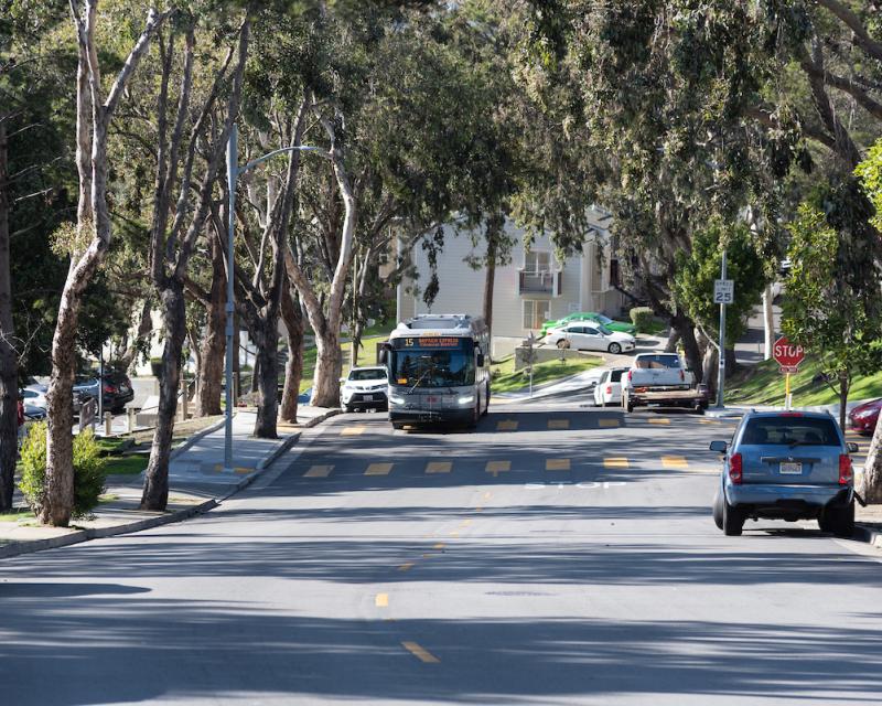 A 15 Bayview Hunters Point Express bus rides down a tree-lined street in San Francisco.