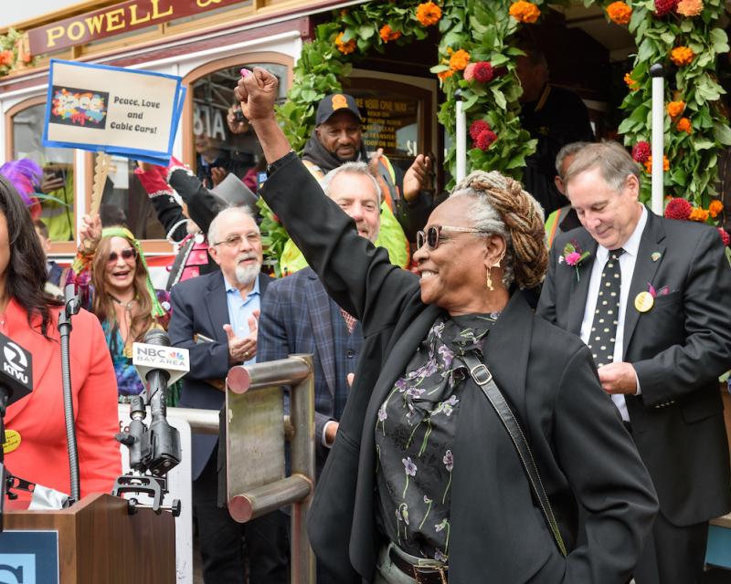 People celebrating in front of a decorated San Francisco cable car and a woman standing in front holding her fist in the air.