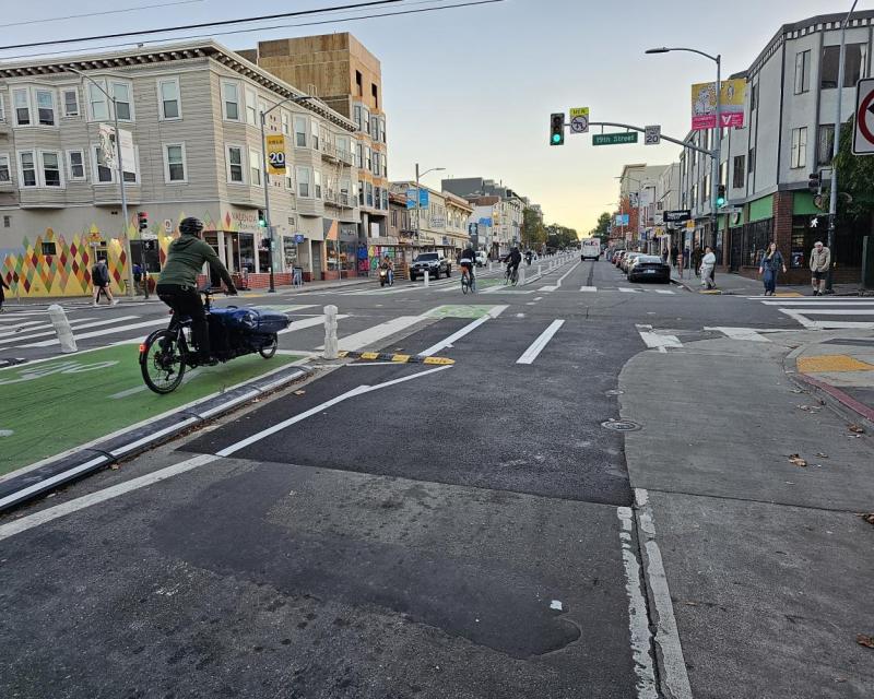 A woman rides a bike on the green, center-running bikeway on Valencia. Cars and other cyclist access the corridor.