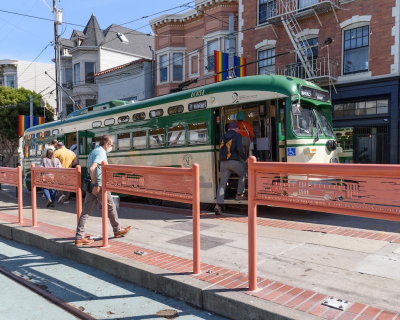 People, a platform, a streetcar and buildings in the daytime. 