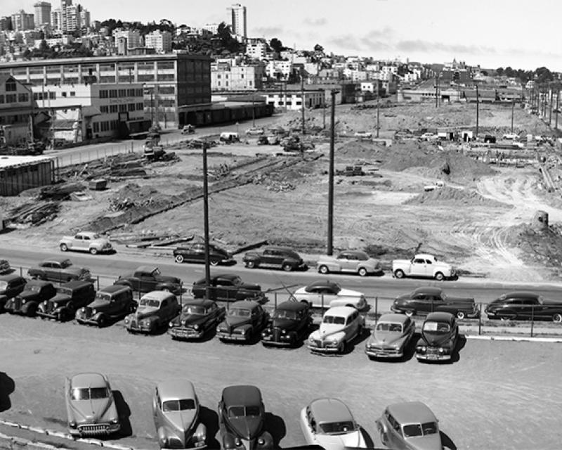 Black and white photo of Kirkland Yard. Dirt covers most of site during construction. Classic cars are parked nearby.