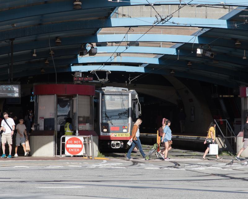 As a K Ingleside train waits to exit West Portal Station, people walk in the crosswalk in front of the station.